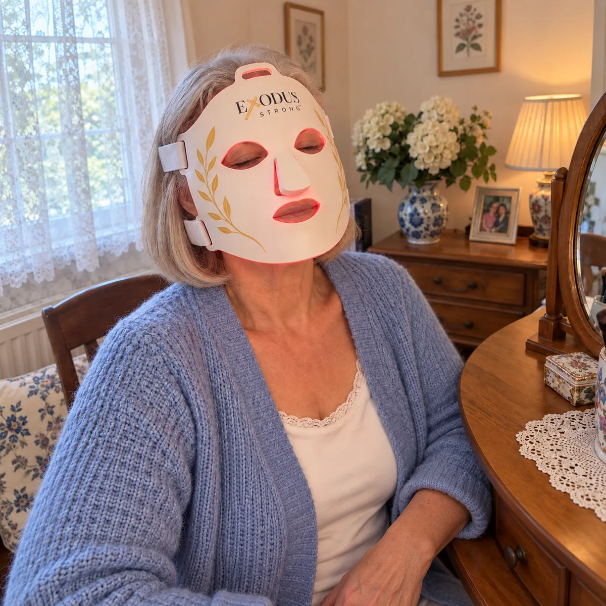 A silver-haired woman at her dressing table wearing the white Red Light+ Face Mask