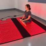 A woman seated cross-legged on an open Red Light+ Blanket