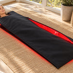 A woman lying inside the Red Light+ Blanket, head out, awake, in a bright sunroom