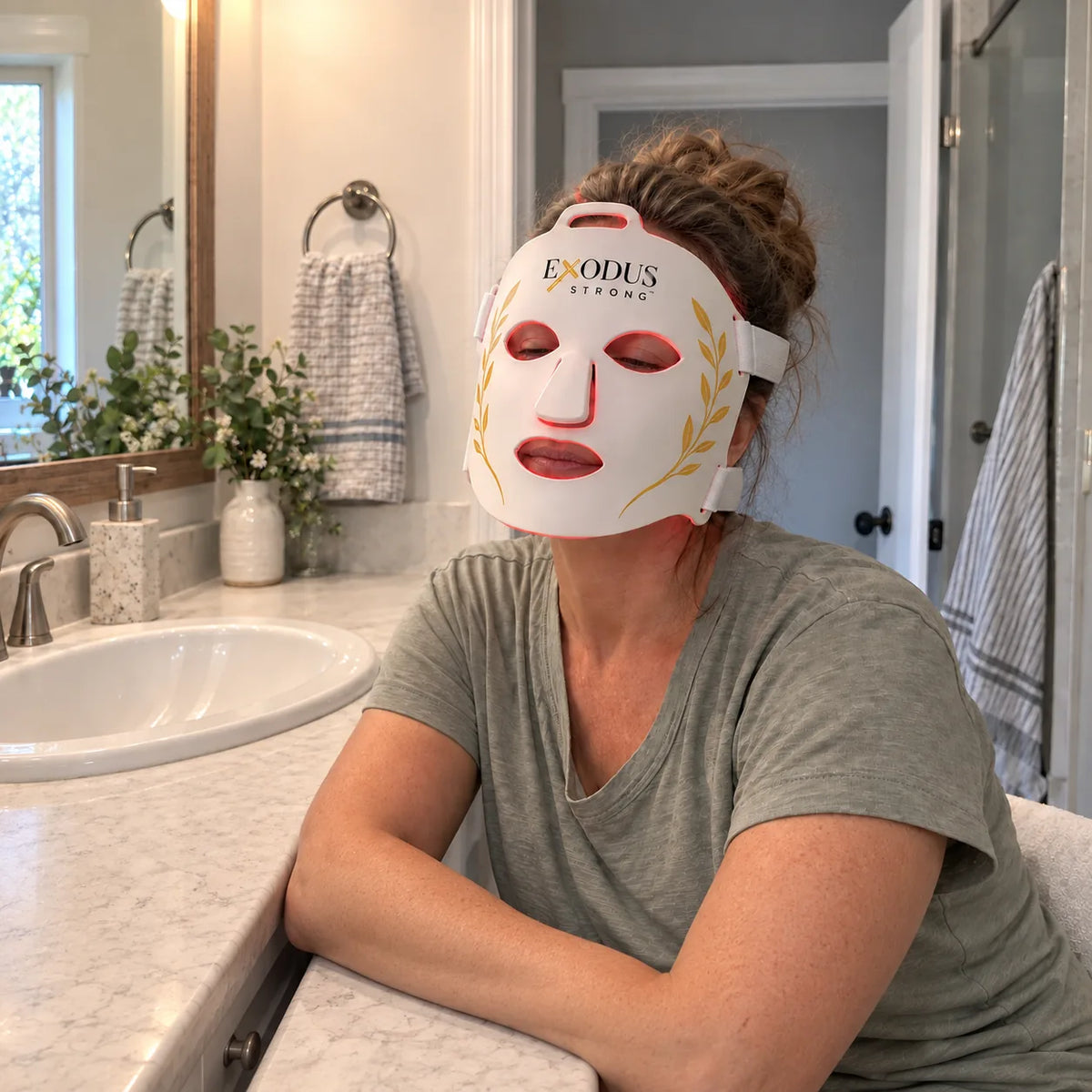 A woman at her bathroom counter in the morning wearing the white Red Light+ Face Mask