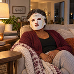 A woman relaxing on her sofa in the evening wearing the white Red Light+ Face Mask