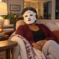 A woman relaxing on her sofa in the evening wearing the white Red Light+ Face Mask
