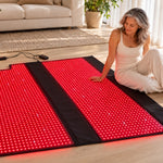 A woman seated beside the open Red Light+ Laser Blanket in a bright living room