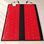 Red Light+ Laser Blanket opened flat on a studio floor, both panels lit, the laser modules showing as brighter points